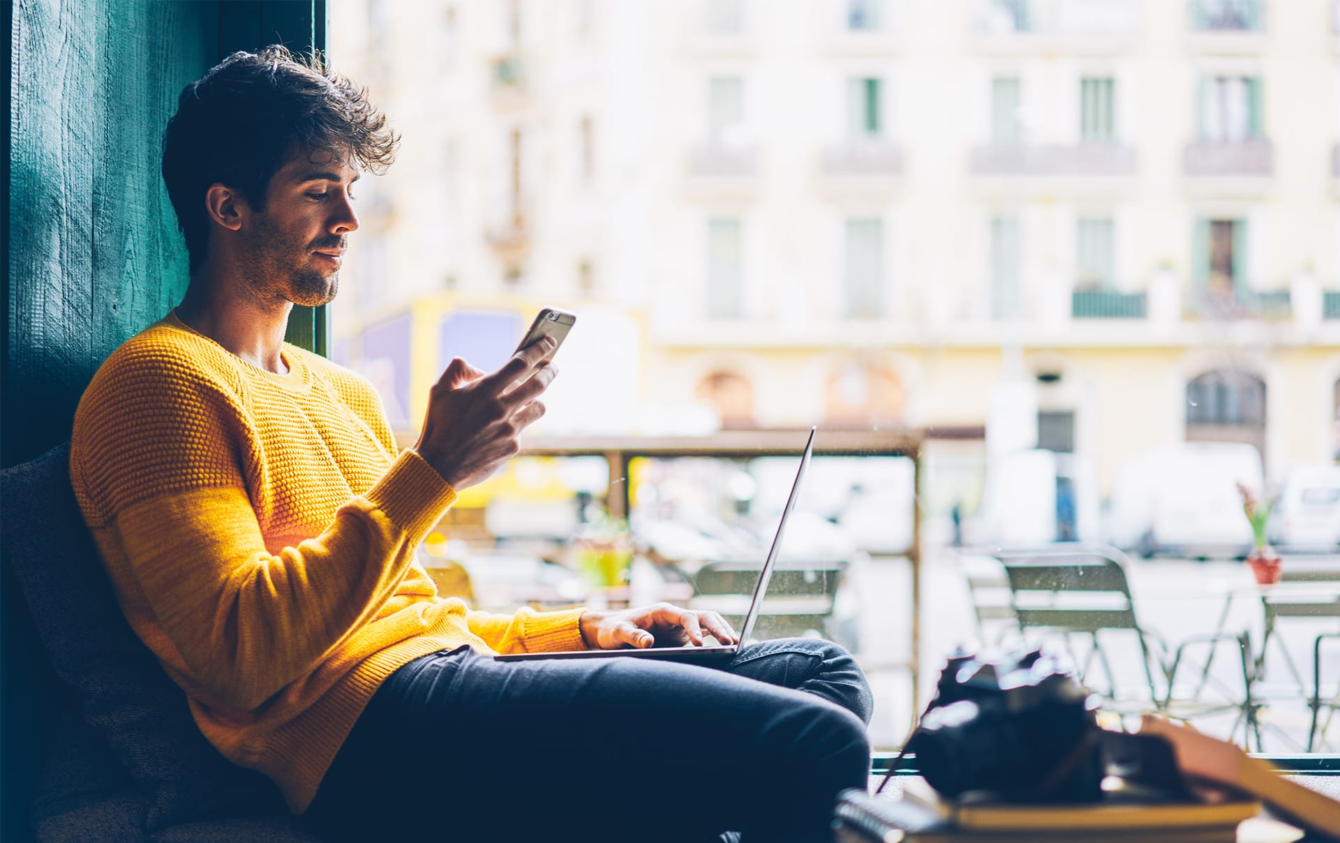 A man looks at his cell phone while his laptop is on his lap