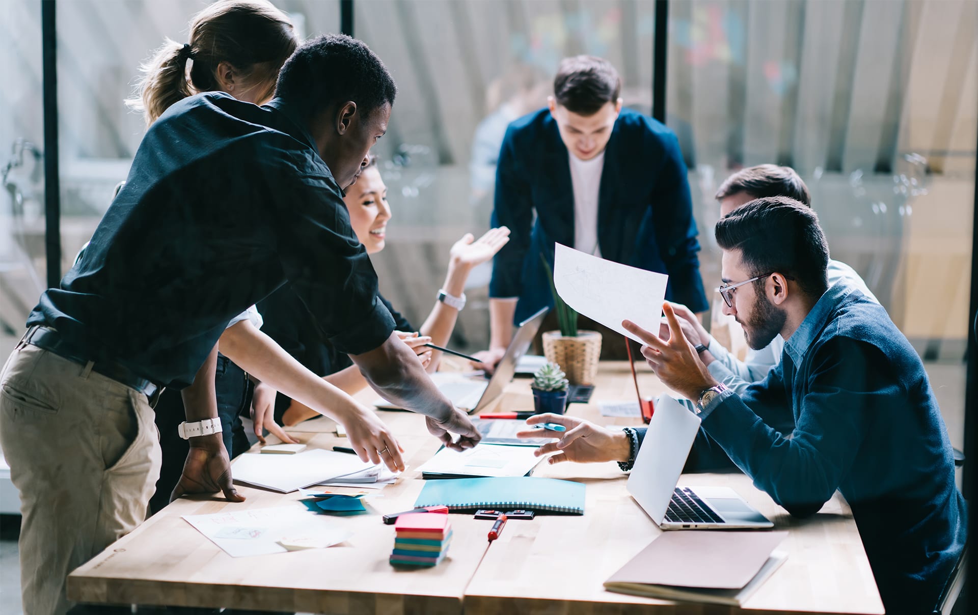 A team of people collaborate over a table with papers and laptops and pens