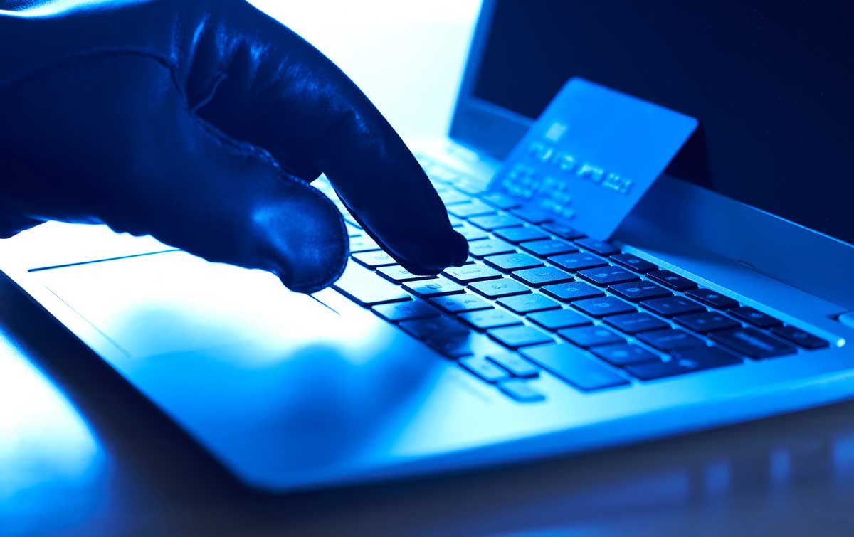 A gloved hand types on a laptop's keyboard with a credit card resting on the laptop